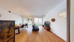 Ett modernt vardagsrum med ett matbord i trä, svarta stolar, en grå soffa och en tv-apparat placerad på ett träskåp.