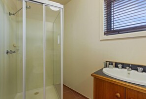A bathroom with a glass shower enclosure, a sink with a wooden vanity, and a window with blinds. - Alpine Heights 14 - Mt Hotham (Hotham Heights)