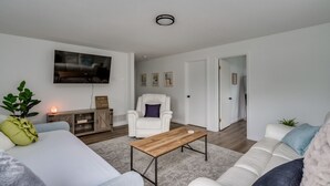 Una sala de estar moderna con un sofá, una mesa de centro, un sillón blanco y un televisor montado en la pared.