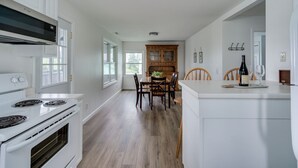Una cocina con armarios blancos, una estufa y un comedor con sillas de madera y una mesa.