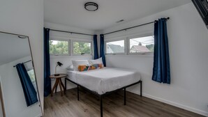 Un dormitorio con cama, una mesita, una lámpara y una ventana con cortinas.