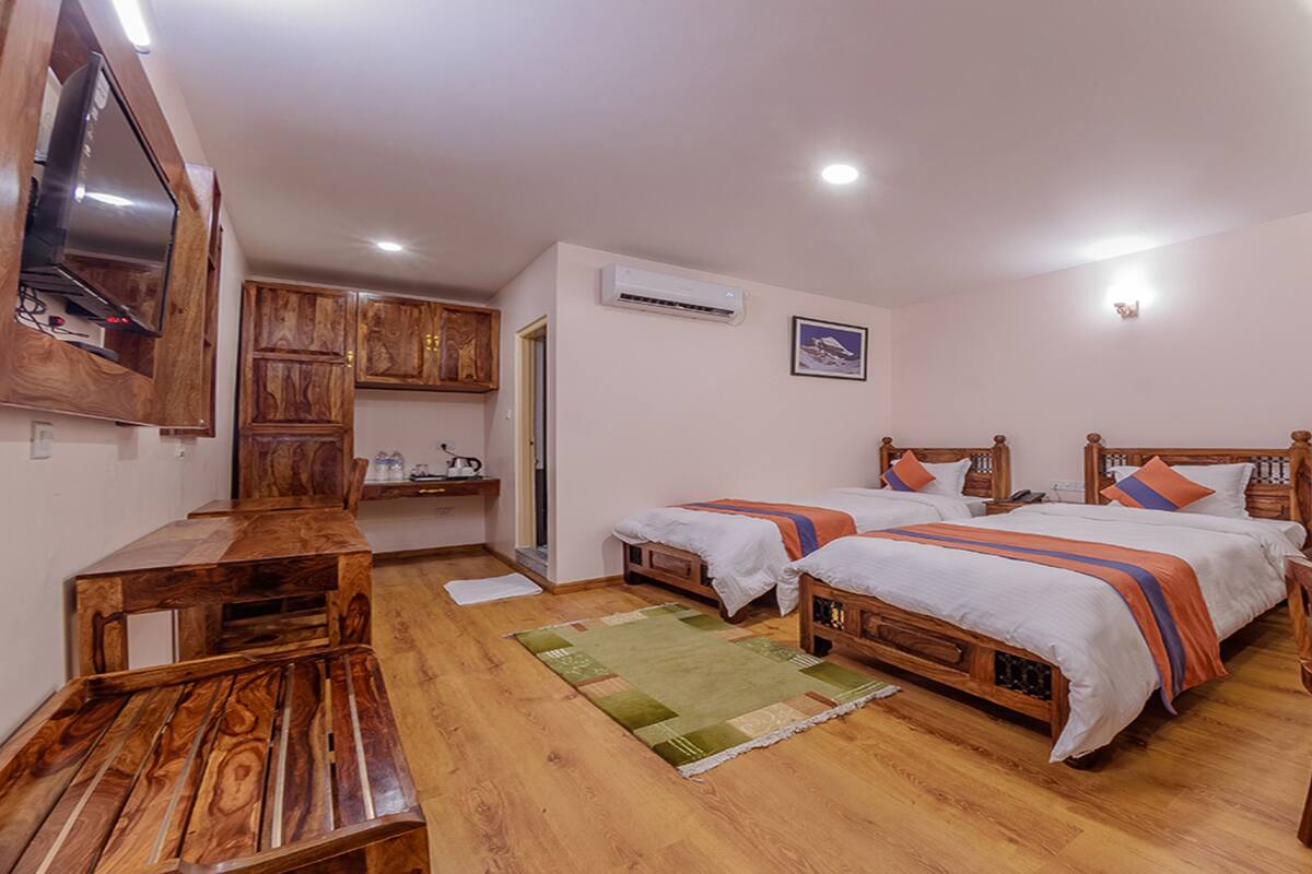 Une chambre avec deux lits, des meubles en bois, une télévision et un appareil de climatisation.