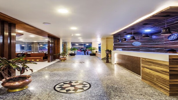A hotel lobby with a reception desk, potted plants, and a patterned floor. - MeroStay 159 Hotel AP (Kathmandu)