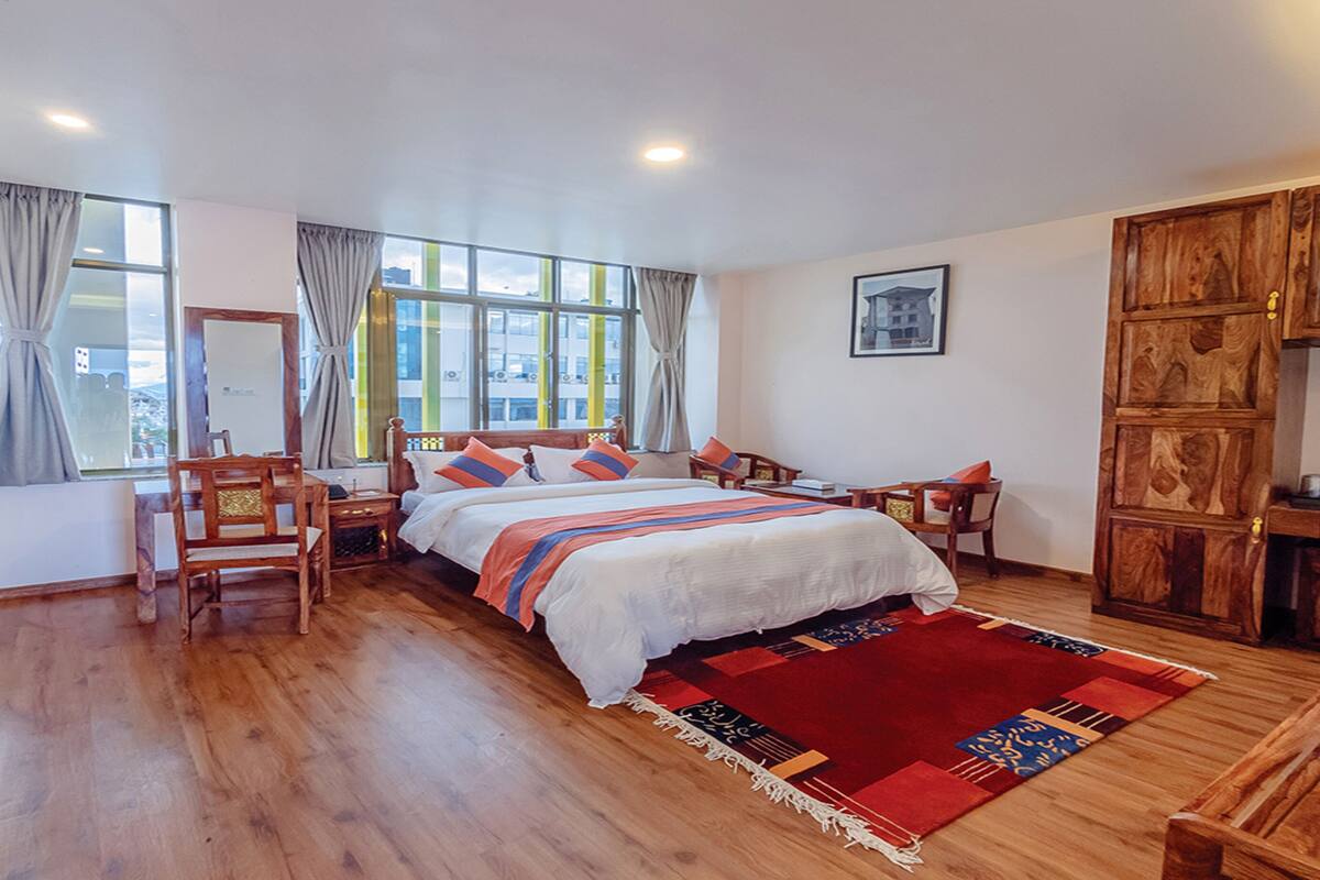 Une chambre d’hôtel avec un grand lit, des meubles en bois, un bureau et une vue sur la ville par la fenêtre.