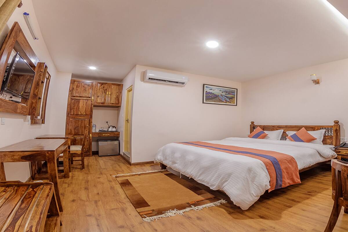 Une chambre d’hôtel avec un plancher en bois, un lit recouvert d’une courtepointe à rayures, un bureau avec une chaise, une petite kitchenette et un appareil de climatisation.