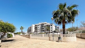 A modern apartment building with balconies, a paved walkway, and palm trees. - Global Vacacional: Apartment with large terrace in Canet (Canet d´en berenguer)