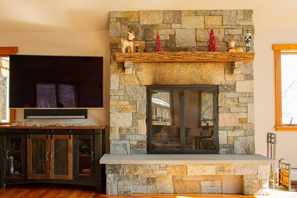 A stone fireplace with a wooden mantel shelf, a TV mounted above, and a stone cabinet below.