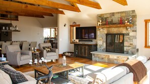 A spacious living room with a stone fireplace, wooden beams, and comfortable seating. - Mountainside 5-BR Ski-In/Out Okemo Retreat (Ludlow)