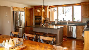 A kitchen with wooden cabinets, stainless steel appliances, and a large island with bar stools. - Mountainside 5-BR Ski-In/Out Okemo Retreat (Ludlow)