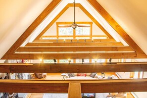 A high-ceilinged room with a sloped wooden ceiling, a ceiling fan, and a window providing natural light.