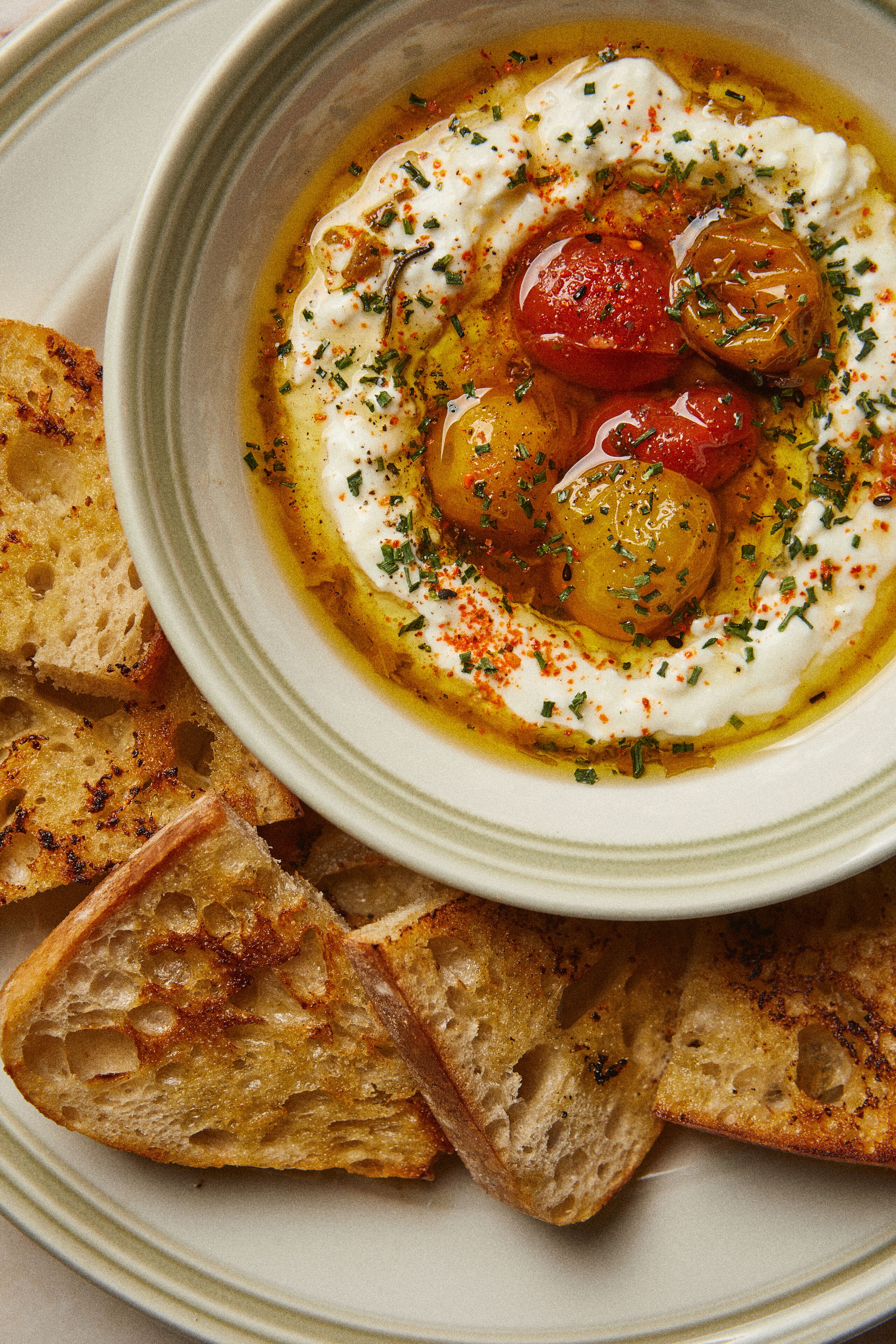 Una ciotola di cibo con pomodori e salsa cremosa, servita con fette di pane tostato.