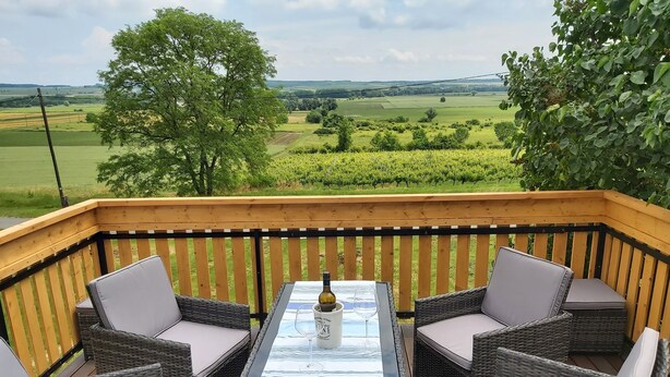 A wooden deck with wicker furniture and a table, overlooking a green landscape. - 1 Bedroom Private vacation home in Vaskeresztes (Vaskeresztes)