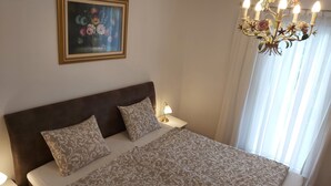 A bedroom with a large bed, two pillows, a nightstand with a lamp, a painting on the wall, and a chandelier. - 1 Bedroom Private vacation home in Vaskeresztes (Vaskeresztes)