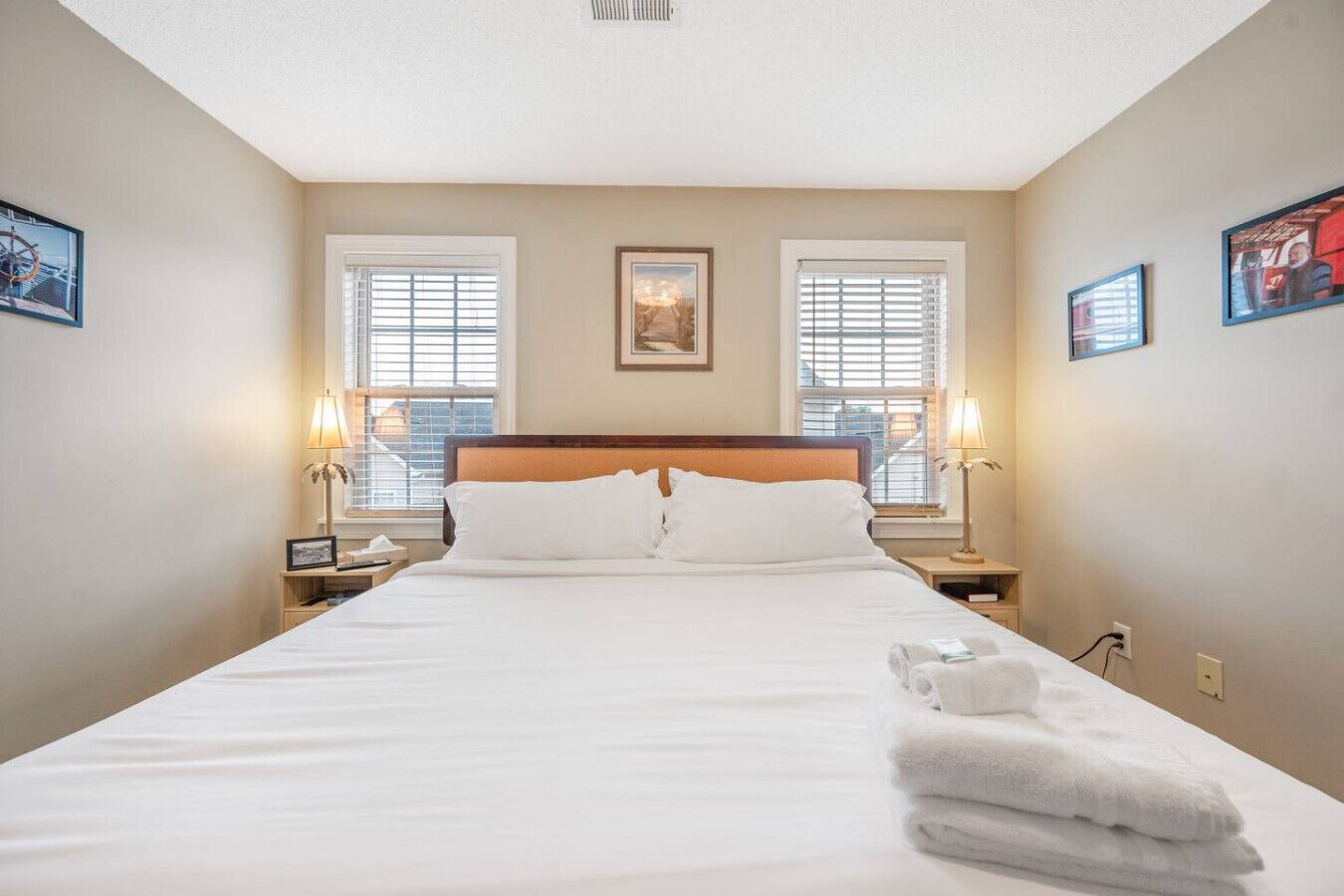 A hotel room with a large bed, two bedside tables with lamps, a window with blinds, and a framed picture on the wall.