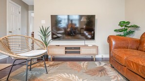 Una sala de estar con una televisión de pantalla plana montada en la pared, una silla de mimbre, un sofá de cuero y un tapete estampado.