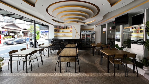 An indoor cafe with wooden tables and chairs, a counter with a menu, and a view of the street outside. - Royal Vista (Patong)
