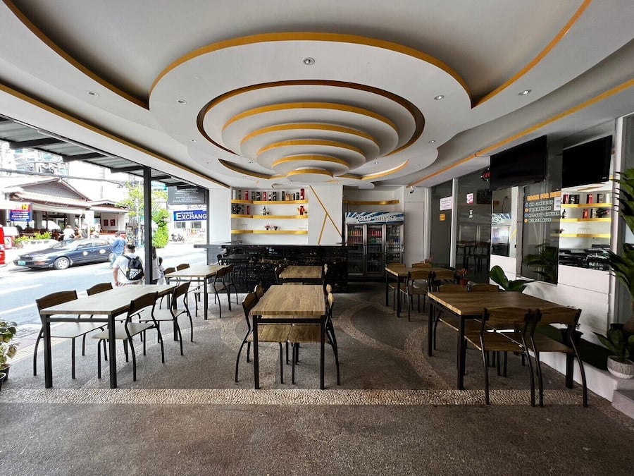 Un café interior con mesas y sillas de madera, una barra con menú y vistas a la calle.