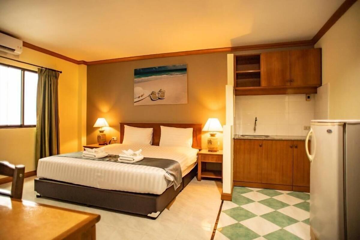 A hotel room with a bed, bedside lamps, a small kitchen area, and a dining table.