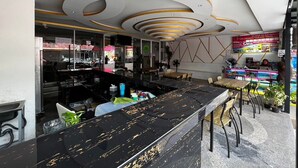 A modern bar area with a black marble countertop, seating with wooden chairs, and a ceiling with circular light fixtures. - Royal Vista (Patong)