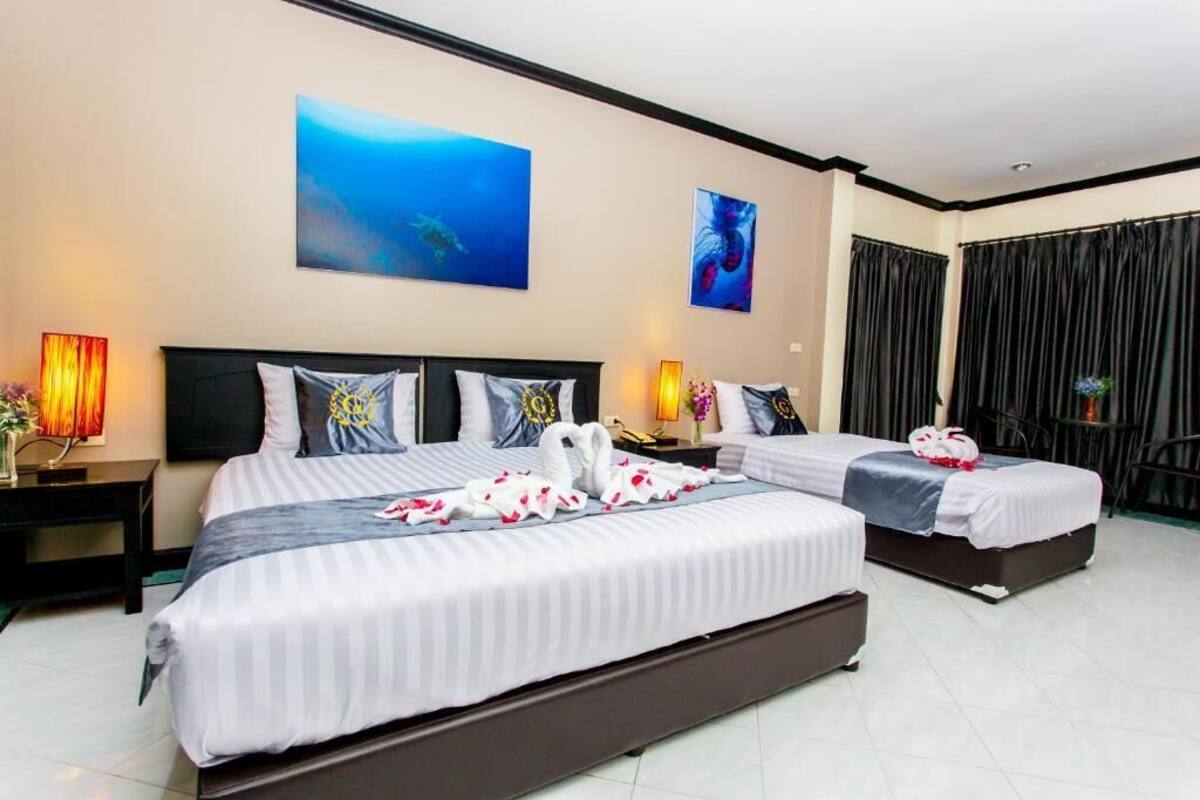 A hotel room with two beds, a large painting of an underwater scene, and a view of the sea through the curtains.