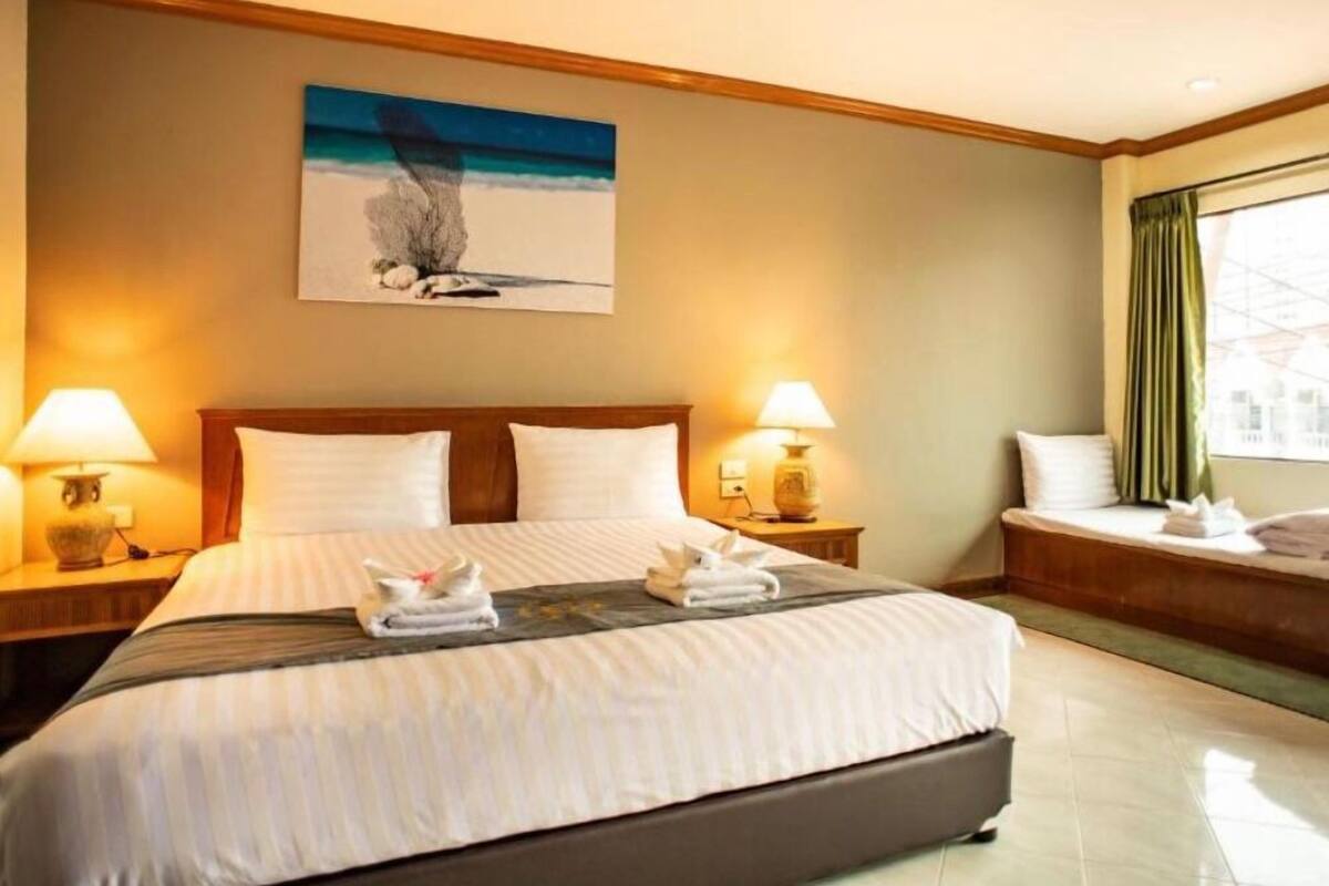 A hotel room with a large bed, two bedside lamps, a painting on the wall, and a window with curtains.