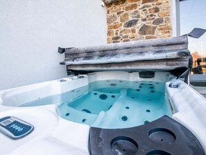 A hot tub with a control panel, set against a stone wall and a white building. - Cozy holiday home in La Reid with a whirlpool (THEUX LA REID)