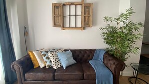 A brown leather sofa with patterned cushions, a wooden wall-mounted shelf, and a bamboo plant. - Nice apartment in the center of Santander (Santander)