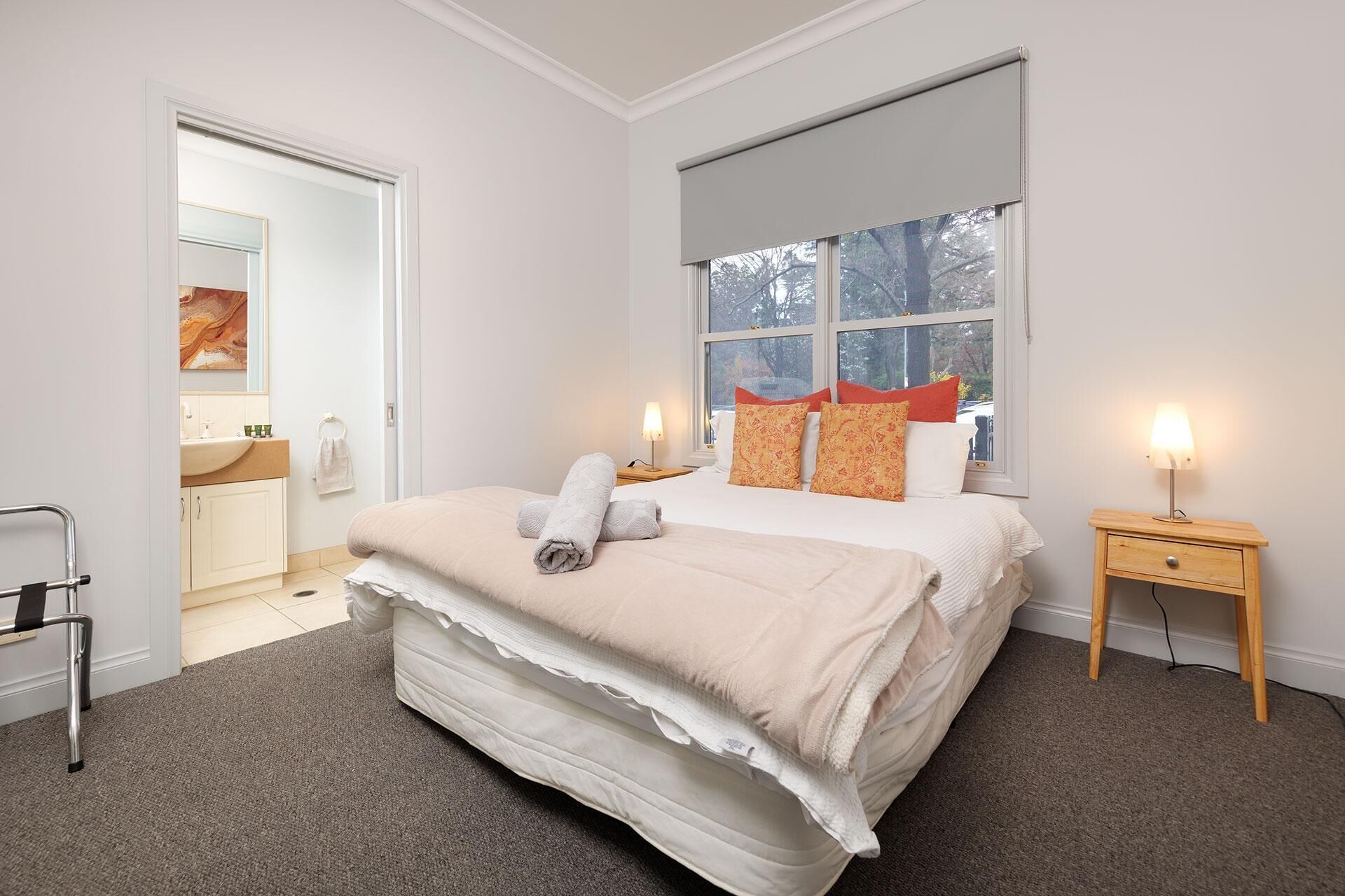 A bedroom with a large bed, two bedside tables with lamps, a window with a view, and a bathroom visible through an open door.