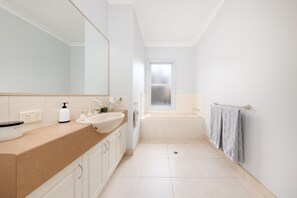 Un baño moderno con un espejo grande, dos lavamanos, una bañera y una ventana.
