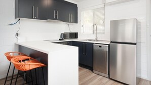 A modern kitchen with dark cabinets, a white countertop, a stainless steel refrigerator, a dishwasher, and two orange bar stools. - Charlie's on Stanley - Cosy one bedroom apartment in the centre of Albury (Albury)