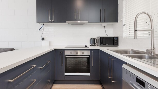 A modern kitchen with dark cabinets, a stainless steel sink, a microwave, and an oven. - Charlie's on Stanley - Cosy one bedroom apartment in the centre of Albury (Albury)