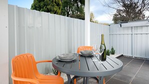 A round outdoor table with two orange chairs, a bottle of wine, and a bowl. - Charlie's on Stanley - Cosy one bedroom apartment in the centre of Albury (Albury)