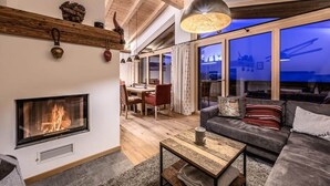 A modern living room with a fireplace, wooden beams, a sofa, and a dining area.