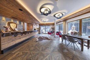 A modern interior with a wooden reception desk, a patterned floor, and large windows offering a view of a forested area.