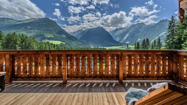 A wooden deck with a view of mountains and a clear sky.