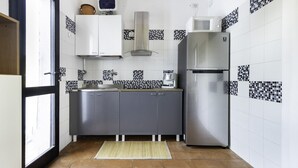 Eine kompakte Küche mit grauen Schränken, einem Edelstahlkühlschrank, einer Mikrowelle und einer gefliesten Spritzwand.