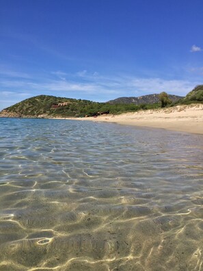 A beach with clear shallow waters, sandy shore, and a hill with vegetation and buildings in the background. - Cozy little house just a 5-minute walk from the beautiful beach at Geremeas (Geremeas)