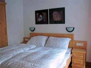 Quarto com uma cama de casal, duas mesas de cabeceira, um painel de madeira na cabeceira e duas luminárias na parede.