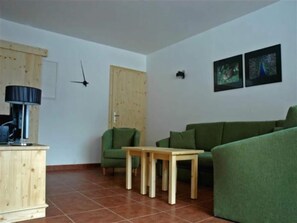 A living room with a green sofa, a wooden table, a lamp, and two framed pictures on the wall.