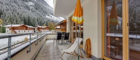 A balcony with a view of snow-covered mountains, a wooden deck, and a lounge chair.