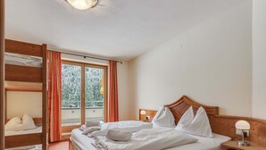 Ett hotellrum med en säng i trä, ett nattduksbord, en lampa och en skjutdörr i glas som leder ut till en balkong.