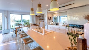 A modern kitchen with a central island, stainless steel appliances, and pendant lighting. - Oriwa Villa, Oneroa Village - near Mudbrick and Cable Bay - Welcome to Oriwa Villa, a luxurious 4 bedroom, 3 bathroom family home. This exquisite holiday home is designed to provide the perfect getaway, offering a blend of elegance, modern amenities, (Waiheke Island)