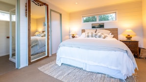 A bedroom with a large bed, two bedside tables with lamps, a window, and a mirror. - Oriwa Villa, Oneroa Village - near Mudbrick and Cable Bay - Welcome to Oriwa Villa, a luxurious 4 bedroom, 3 bathroom family home. This exquisite holiday home is designed to provide the perfect getaway, offering a blend of elegance, modern amenities, (Waiheke Island)