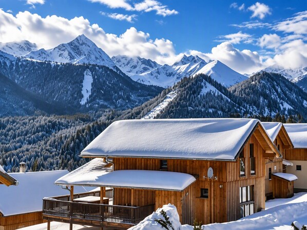 Una cabaña de madera con balcón, rodeada de montañas y árboles cubiertos de nieve.