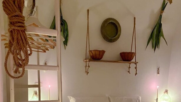Una camera da letto accogliente con un letto, comodini, una pianta sospesa e uno scaffale con oggetti decorativi.