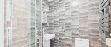 A bathroom with a shower, toilet, and sink, featuring a patterned tile wall.