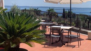 Un patio al aire libre con mesas y sillas, una sombrilla blanca y vista al mar.