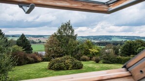 Une vue depuis une fenêtre donnant sur un paysage verdoyant, avec des arbres et des champs.