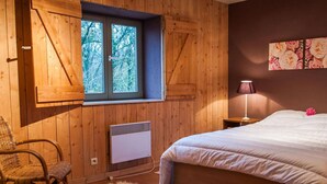 Une chambre avec un grand lit, une fenêtre donnant sur des arbres, une chaise, un radiateur et une lampe.