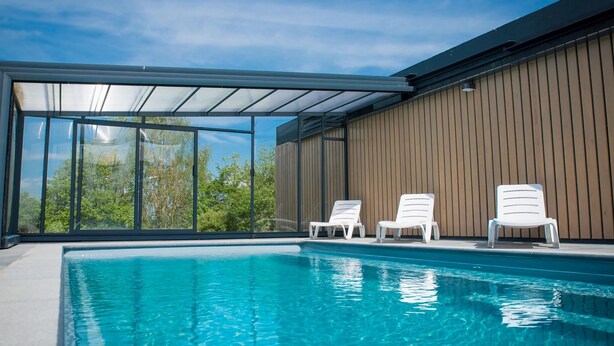 Une piscine  à l’eau d’un bleu cristallin, entourée d’un mur en bois et protégée par une paroi de verre.